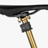 An Apidura Backcountry Dropper Post Adapter is shown mounted to a polished gold seatpost underneath a saddle