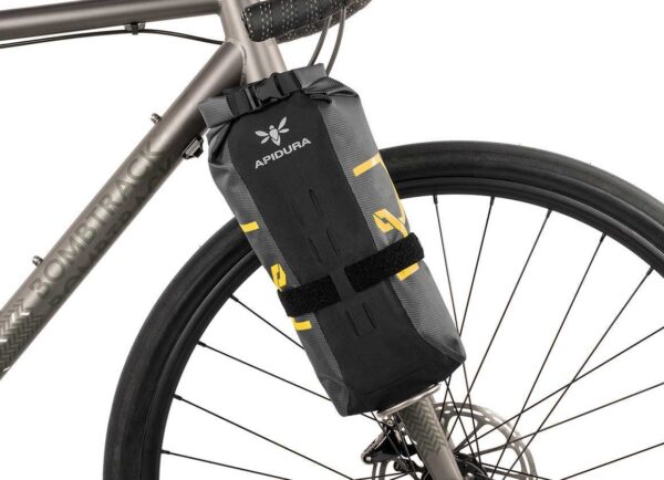 An Apidura Expedition Fork Pack 3L is shown in a black & grey waterproof laminate material, mounted to the fork of a bicycle