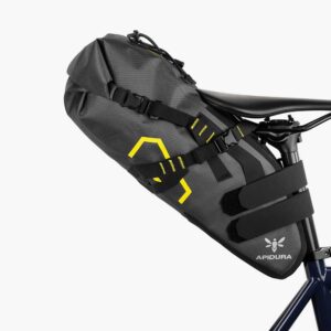 An Apidura Expedition Saddle Pack is shown mounting to the saddle & seatpost of a bicycle with two velcro straps & a buckle strap as well as a securing tie down from the roll-closure opening of the bag