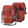 A pair of Ortlieb Bike-Packer Plus waterproof panniers are shown back to back with a Rooibos red colourway and black mounting hardware