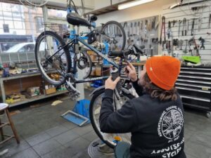 A mechanic is shown working on a bicycle in a workstand inside a workshop performinga Comprehensive Service on a 1990s era mountain bike
