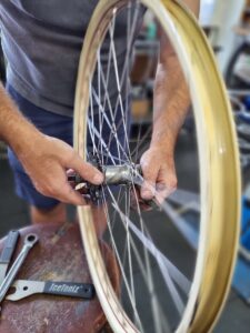 A mechanics is shown holding a coaster brake hub in a vintage steel bicycle wheel that is being rebuilt