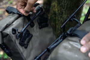 A hand is shown lifting the mounting hook of a QL3.1 Ortlieb Gravel pack pannier from their bike rack